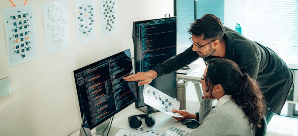 Software developer pointing at code on a screen, showing co-worker