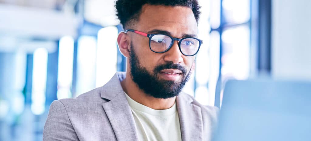 Man with beard wearing glasses looking at blurred out laptop