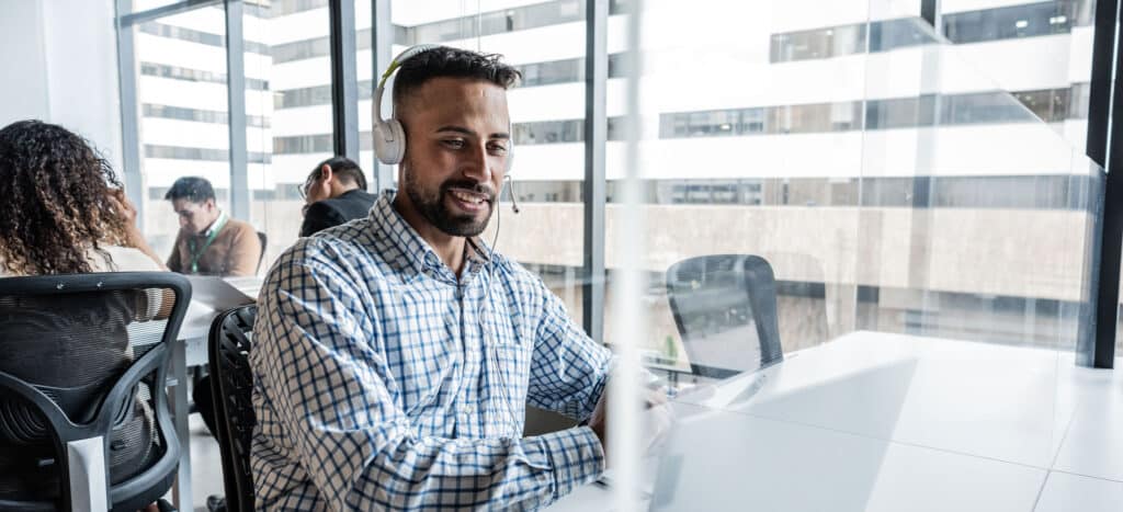 Man wearing headset with microphone smiling at laptop