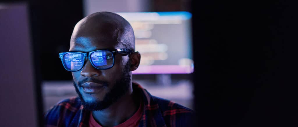 Cybersecurity professional staring a computer with the screen reflecting in his glasses