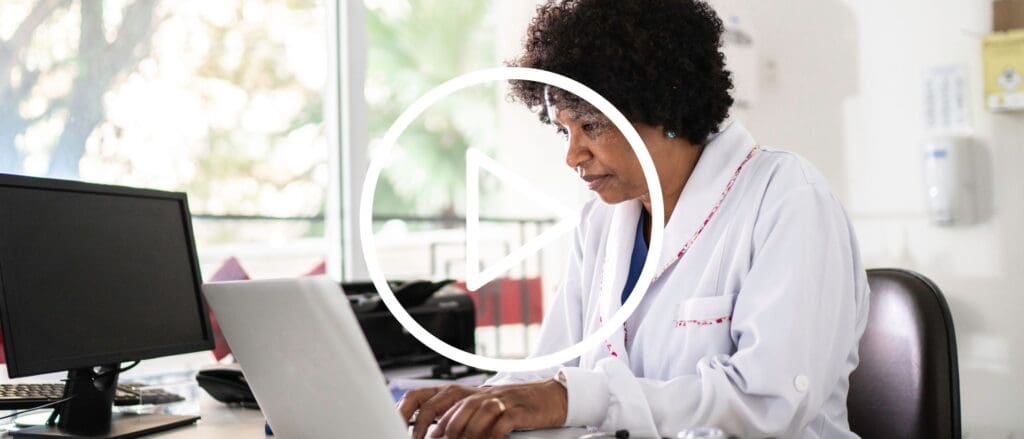 Nurse Practitioner typing on laptop in office setting, with 'video play' button overlay