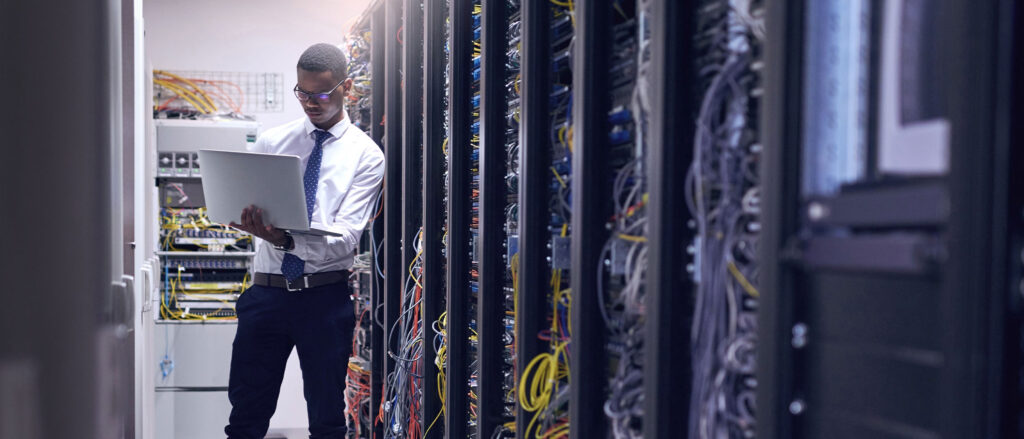 Man standing in server room, holding laptop