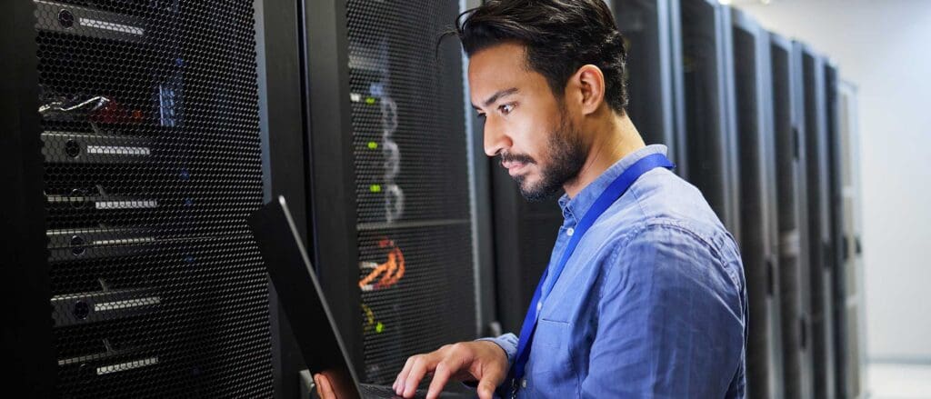 Man in a server room, holding a laptop