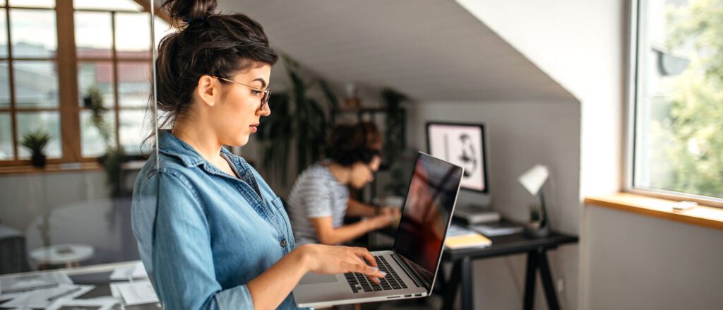 Woman working on laptop while holding it, standing up