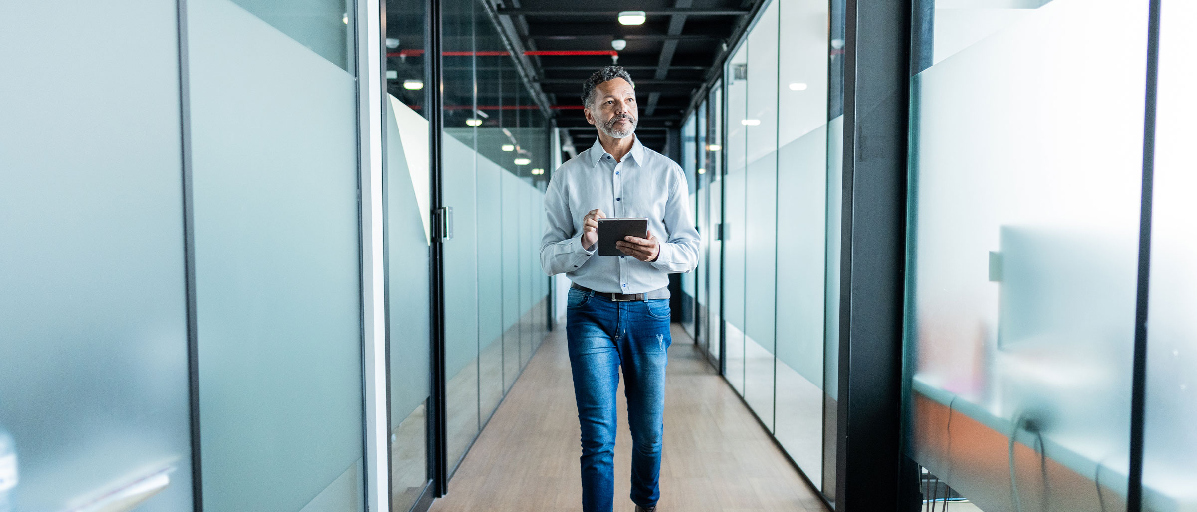 Man walking down hallway with tablet in hand