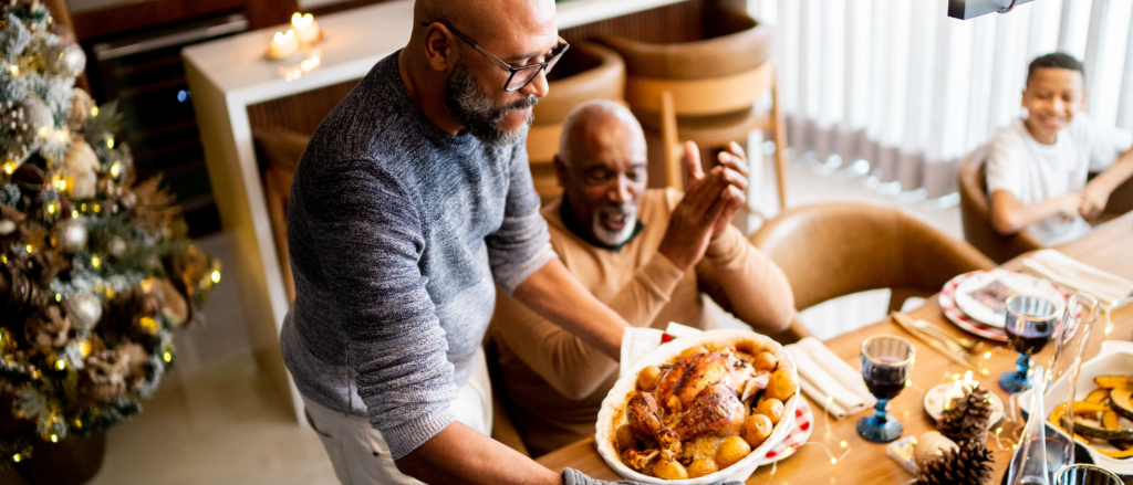 Man putting thanksgiving turkey down on table, with family sitting around