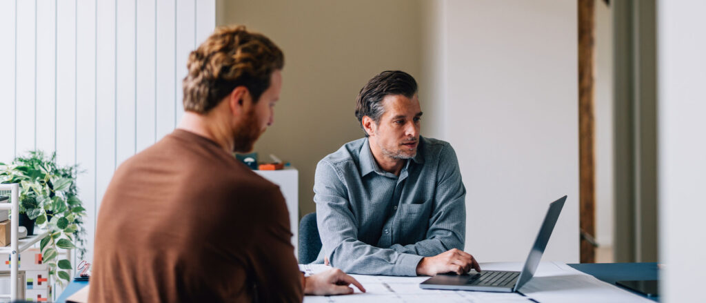 Two men sitting at a table inspecting what is on a laptop