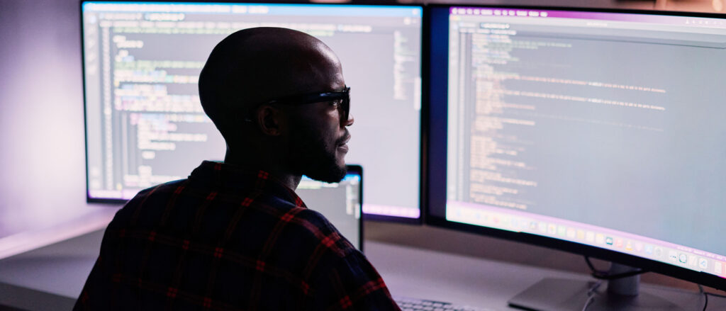 Man looking at code on two monitors