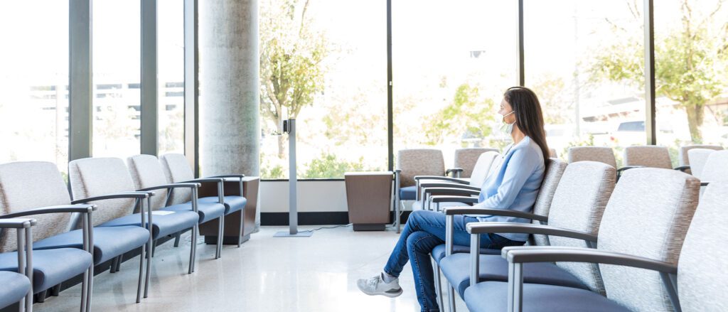 Woman wearing a mask sitting in the waiting room of a doctors office