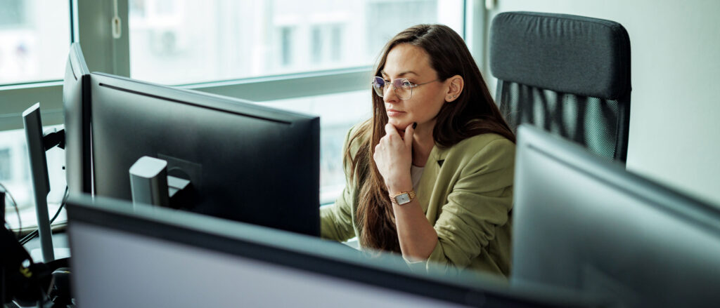 Woman sitting at desk working from two monitors