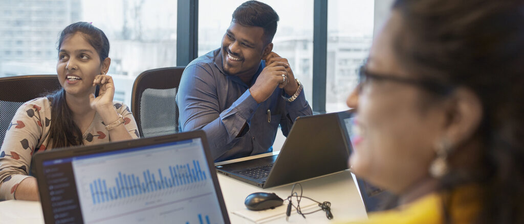 Woman out of focus looking at laptop with bar chart. Another woman and man smiling in the background